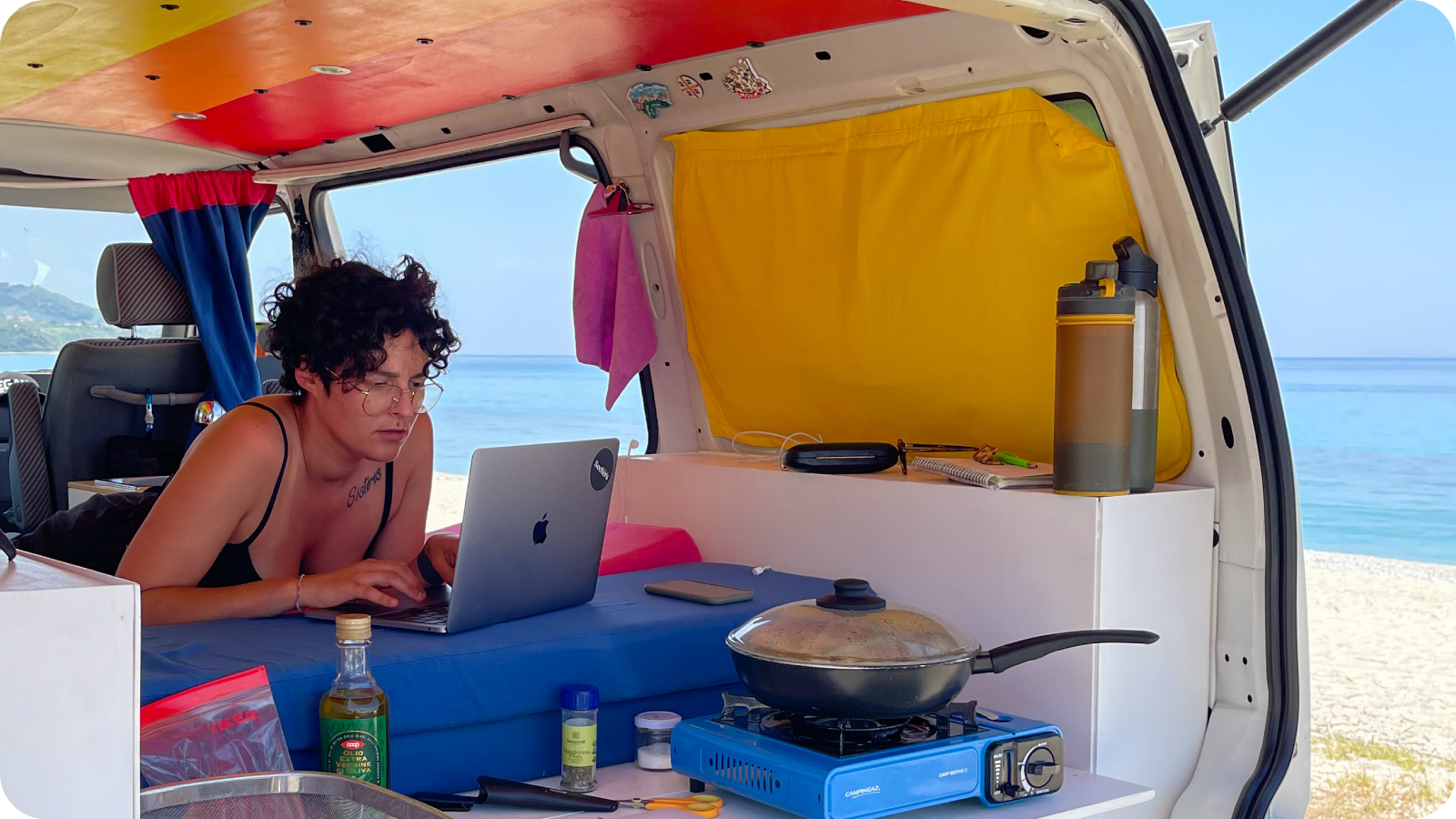 Angie is working on the van, sea side, while Mat is cooking.